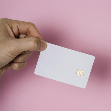 A hand holding a blank white SIM card on a vibrant pink background, showcasing technology.
