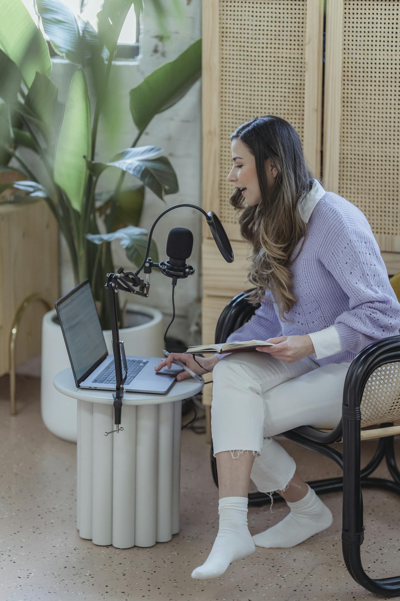 Female podcast host sitting with a laptop and microphone, recording content indoors.